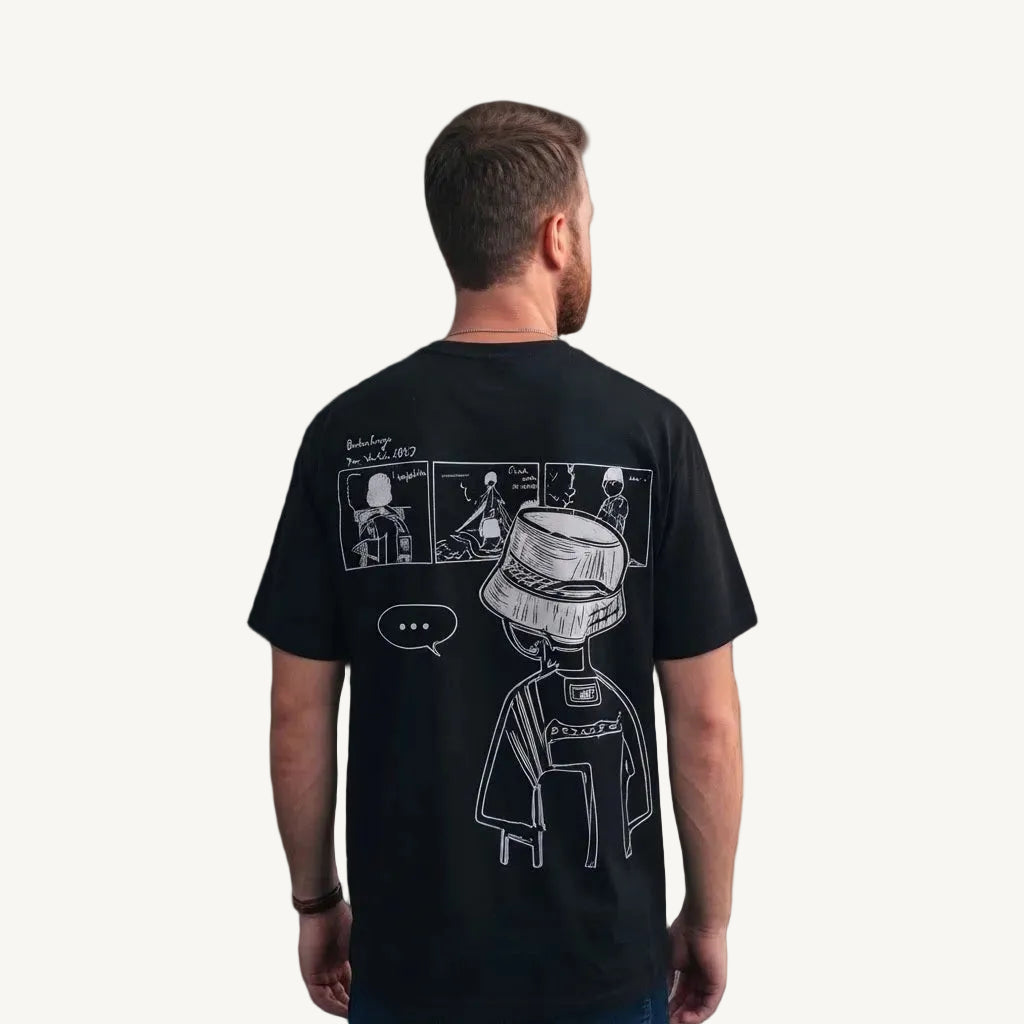 A man viewed from behind wearing a black t-shirt with a white line-art graphic of a character in a bucket hat and comic panels on the back, set against a plain gray background.