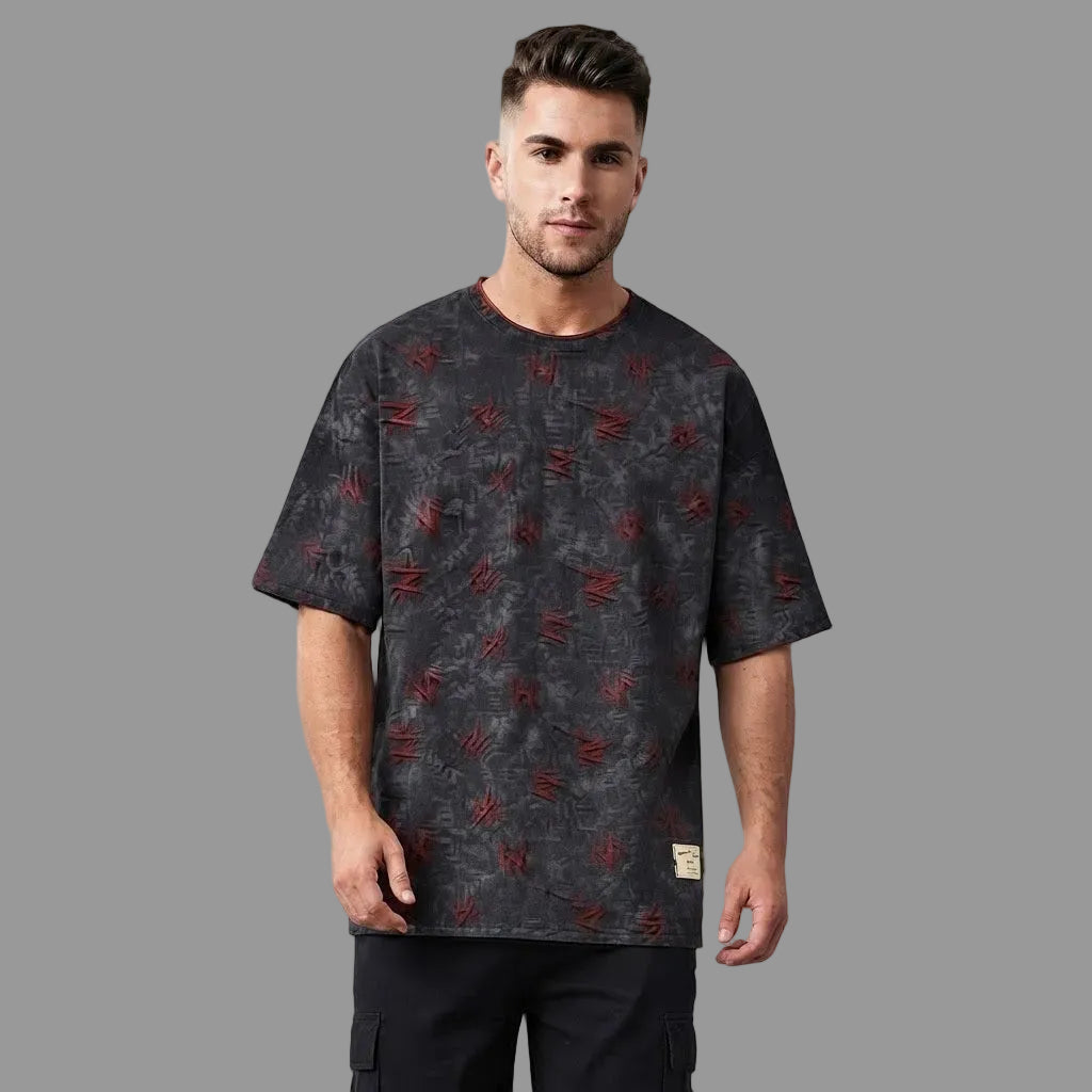 A man wearing a dark gray short-sleeve t-shirt with a distressed red graphic pattern, standing against a solid gray studio background.