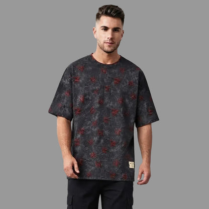 A man wearing a dark gray short-sleeve t-shirt with a distressed red graphic pattern, standing against a solid gray studio background.
