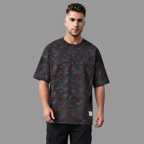 A man wearing a dark gray short-sleeve t-shirt with a distressed red graphic pattern, standing against a solid gray studio background.