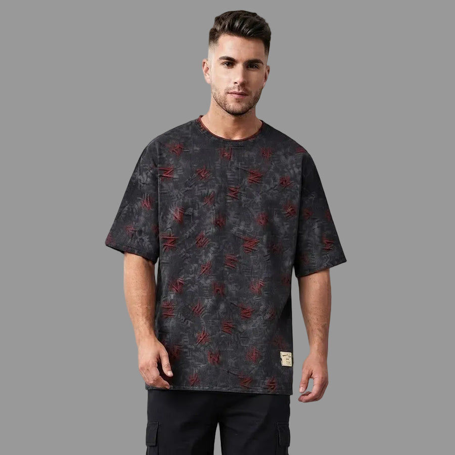 A man wearing a dark gray short-sleeve t-shirt with a distressed red graphic pattern, standing against a solid gray studio background.